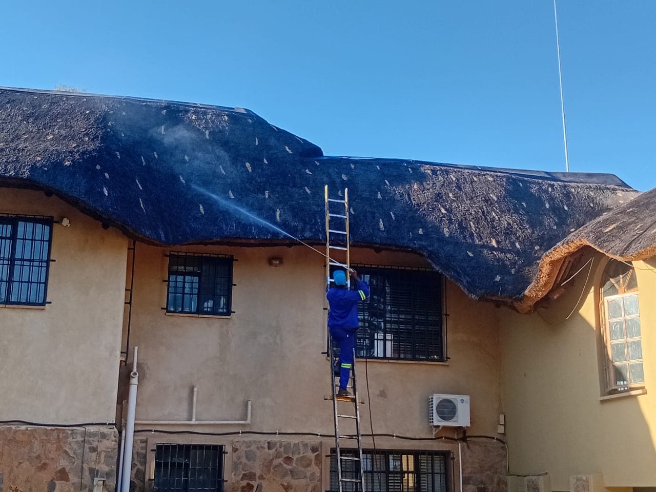 Thatch roof being cleaned and treated with a spray application