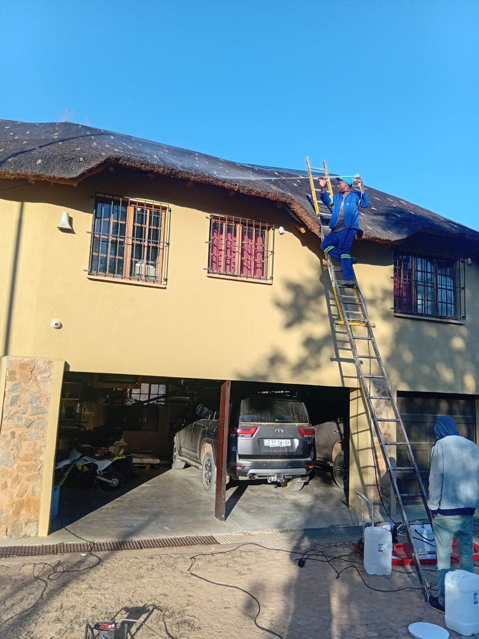 Thatcher on a ladder carrying out thatch roof maintenance